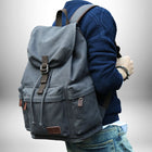Un homme porte un sac a dos coton gris avec des détails en cuir, il porte un pull bleu et un jean. — vue 6