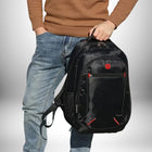 Un homme portant un sac à dos noir avec des accents rouges, avec une main dans sa poche et une autre tenant le sac. Il porte un pull marron et un jean bleu. L'arrière-plan est dégradé du blanc au gris.
— vue 7