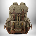 Un sac à dos en toile de couleur olive avec des garnitures en cuir marron, des boucles et des sangles, avec un compartiment principal à cordon et des poches latérales.
— vue 2
