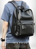L'image montre un homme portant un sac dos cuir homme noir. Le sac a une poche avant et des sangles réglables. L'homme porte un t-shirt bleu clair et une montre noire. Un tatouage est également visible sur son bras. — vue 2