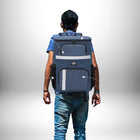 Un homme vu de dos porte un grand **sac a dos pique nique** bleu sur le dos. Le sac a des poches latérales noires et des bandes réfléchissantes. — vue 2