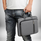 Un homme porte une sacoche ordinateur homme tendance grise devant lui. Il porte un jean délavé et un t-shirt blanc.
— vue 3