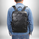 Gros plan d'une personne portant un sac à dos en cuir noir, vue de dos, avec un jean bleu et une chemise en jean. — vue 3