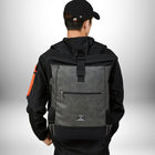 A person wearing a black jacket, black baseball cap, and a grey and black backpack. The backpack has a zipper pocket and a small logo. The person is facing away from the camera. — vue 3