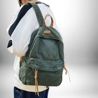 Une personne porte un sac a dos coton vert avec des lanières en cuir. La personne porte un pull blanc et noir avec un jean bleu.
— vue 5
