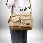 Un jeune homme porte un sac de ville homme. Le sac est de couleur beige avec plusieurs poches sur le devant.
— vue 2
