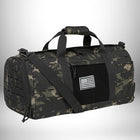 Un sac de sport militaire de couleur noire avec un motif de camouflage est posé devant un fond dégradé. Le sac est équipé de multiples compartiments, d'une bandoulière et d'une poignée supérieure. Un drapeau américain est cousu sur une surface velcro du sac. — vue 8