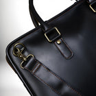 Close-up of a black leather briefcase, showing details like stitching, metal hardware, and a detachable "strap". — vue 6