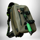 Ce plan rapproché présente un sac de sport imperméable d'une couleur kaki clair. Le sac est doté d'une fermeture éclair verticale, d'une poignée de transport en haut, de sangles et d'une bretelle noire. Une balance à poisson à prise verte est accrochée à des attaches à l’avant du sac. Une plante avec des feuilles est insérée entre la bretelle gauche et le sac.
— vue 3