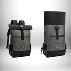 Two modern-looking backpacks are displayed against a white background. The backpacks are in a gray/charcoal color scheme with black accents. The left backpack is closed with a roll-top design, and a black strap with a buckle. The right backpack is open with the roll part in the up position. — vue 5