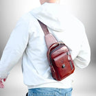 Une personne portant une veste blanche et un sac à bandoulière marron. La personne est vue de dos. Le sac est en cuir et comporte plusieurs compartiments. L'arrière-plan est flou.
— vue 6