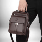 L'image montre une personne tenant un sac en cuir marron. Le sac est carré avec une poignée sur le dessus et une bandoulière. Il y a une poche avant avec un fermoir en métal et une fermeture éclair sur le dessus.  L'arrière-plan est blanc et noir.
 — vue 4