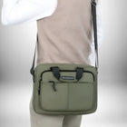 Une personne vue à mi-corps porte un cartable pour enseignant de couleur vert olive sur son épaule. Le sac présente une poche avant zippée et une poignée de transport noire.
 — vue 4