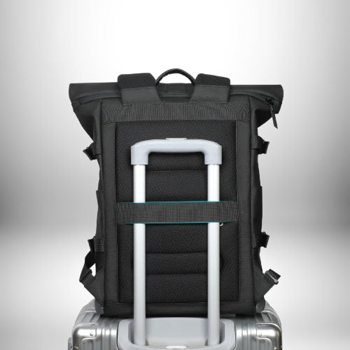 Un sac à dos noir est posé sur le manche d'une valise grise. Le sac à dos est fait d'un matériau noir avec des sangles et des bretelles noires. Il y a une poignée sur le dessus du sac à dos. La valise est en métal argenté et a une poignée rétractable. Le fond de l'image est blanc avec une légère décoloration.