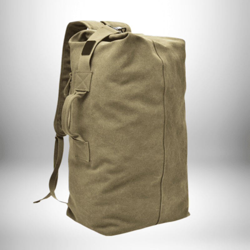 Sac à dos de sport en toile de couleur kaki, sur fond blanc avec un dégradé gris. Le sac est posé sur une surface non visible et offre une vue de trois quarts montrant le côté gauche, le devant et le dessus. On aperçoit une poignée sur le côté et des bretelles. Le sac est vide et non rempli.
