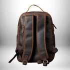 Un sac à dos en cuir marron pour homme avec une poignée supérieure et des sangles de sac à dos. Il est légèrement frotté et vieilli. — vue 4