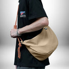 Un homme porte un petit sac de sport homme beige qui contraste avec son t-shirt noir. Le sac a une sangle en corde orange et blanche. Il porte également un bracelet en argent. — vue 6