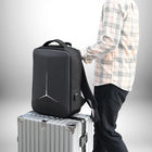 Un homme tient un sac à dos coque rigide noir, posé sur une valise argentée. Le sac à dos est orné d'un motif blanc géométrique. L'homme porte une chemise à carreaux et un pantalon noir. — vue 2