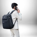 Image d'un homme, dos à la caméra, portant un sac à dos professionnel homme tout en parlant au téléphone. Il porte un costume clair et le sac à dos noir est équipé d'un port USB.
 — vue 2