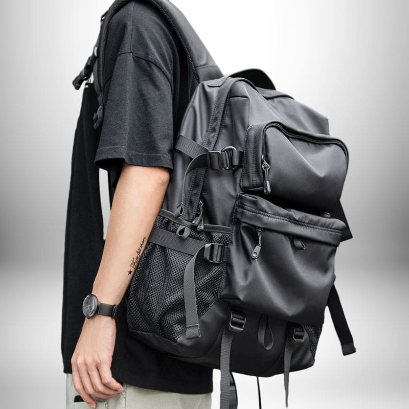 Un homme porte un sac à dos ergonomique noir sur son dos. Le sac à dos a de nombreuses poches et sangles, et semble être fait d'un matériau durable et résistant à l'eau.