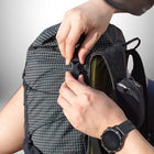 A close-up shot shows two hands buckling the top clasp of a black and white grid backpack with a black watch visible on one wrist. — vue 4