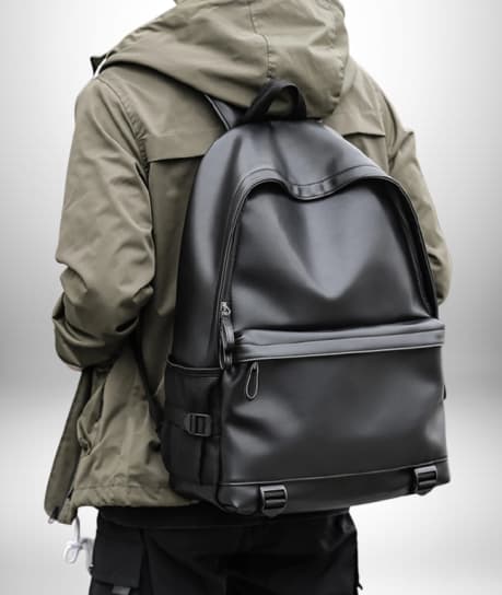 Gros plan d'une personne portant un sac à dos simili cuir homme noir, avec une veste verte à capuche.