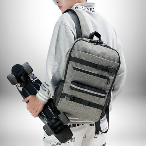 Une personne porte un sac à dos skate et une planche à roulettes, sur un fond flou blanc et gris.
