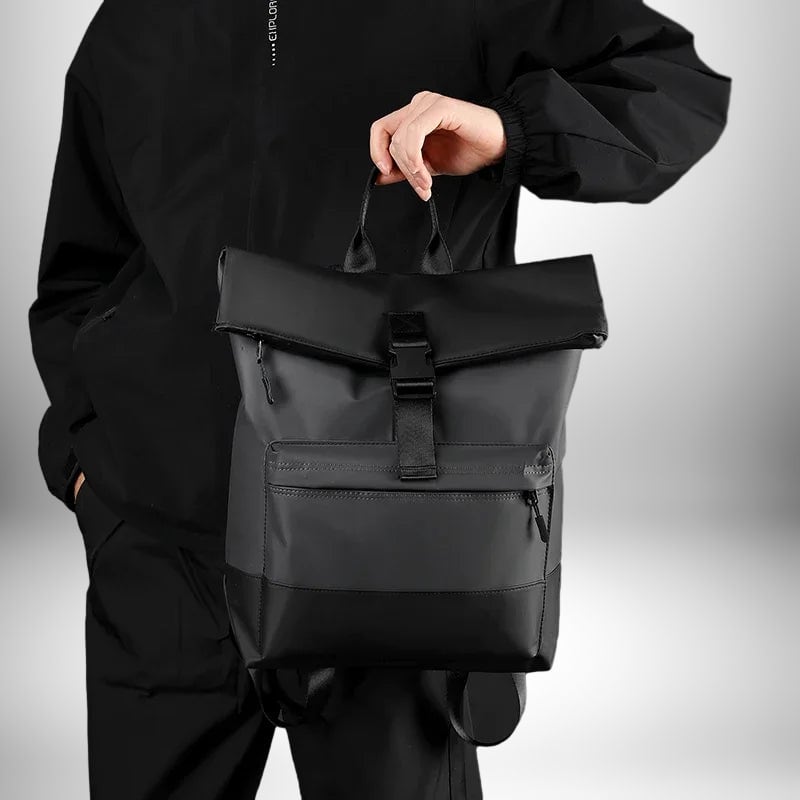 Une personne porte un sac a dos business noir, de style business, sur un fond blanc. Le sac à dos a une poche avant zippée, une boucle de fermeture centrale et une poignée supérieure.