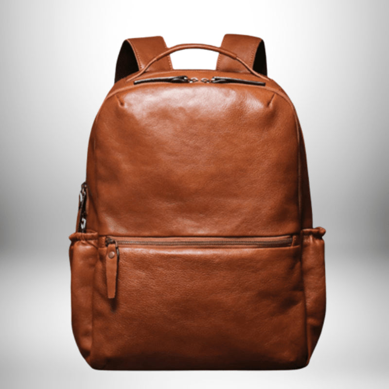 Un sac à dos en cuir marron avec une poignée sur le dessus ainsi que deux bretelles et deux poches zippées.