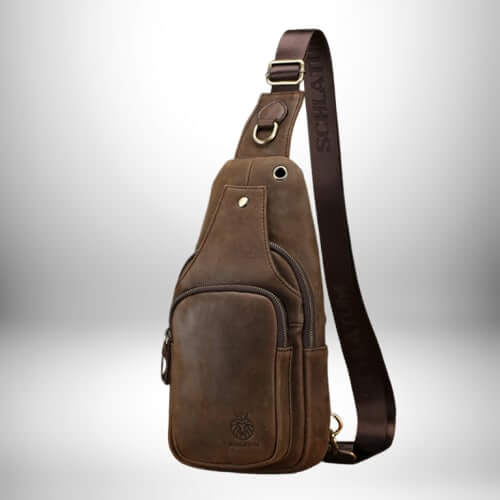 Image d'un petit sac bandoulière cuir marron foncé. Le sac est en cuir vieilli avec une poche zippée sur le devant. La sangle est également en cuir marron avec le nom "SCHIATU" imprimé dessus.