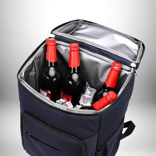 Un sac à dos isotherme bleu foncé ouvert, contenant trois bouteilles de bière avec des bouchons rouges et des glaçons.
