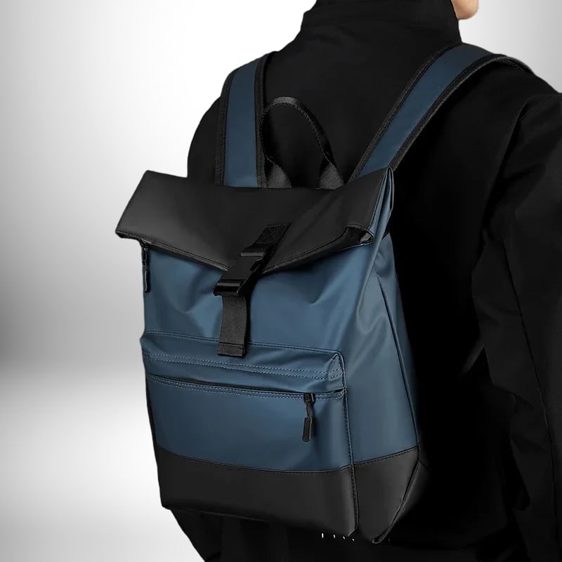 Un sac a dos business bleu et noir est porté par une personne vêtue d'une veste noire. Le sac à dos a une poche avant zippée et une fermeture à boucle.