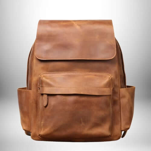 Gros plan d'un sac à dos camel​ en cuir à l'aspect vintage. Le sac à dos est de couleur marron clair avec une poche avant plus petite, des poches latérales et un rabat sur le dessus