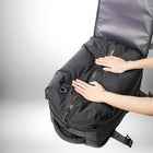 Deux mains touchent un sac à dos noir gonflé avec une ouverture visible. Le sac à dos est noir avec des fermetures à glissière visibles et un bouton noir. Le fond et les sangles du sac à dos sont visibles. L'intérieur du sac à dos est gris. Le texte alternatif pourrait être : Une image d'un sac à dos gonflable contenant un bagage à main easy jet.
 — vue 2