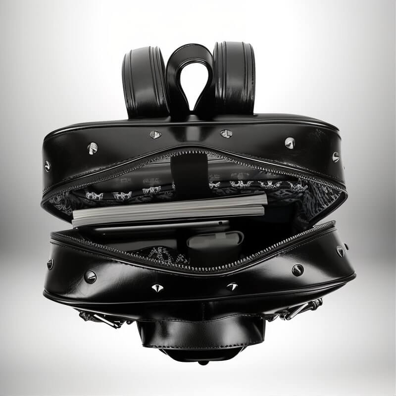 Un sac a dos gothique noir ouvert, avec des rivets métalliques. On peut voir des livres, une tablette et des écouteurs à l'intérieur du sac.