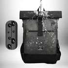A black backpack showing water resistance. Water is being poured onto the backpack, and the droplets are visible on the surface. A cutout on the left illustrates the water resistance of the material. — vue 4