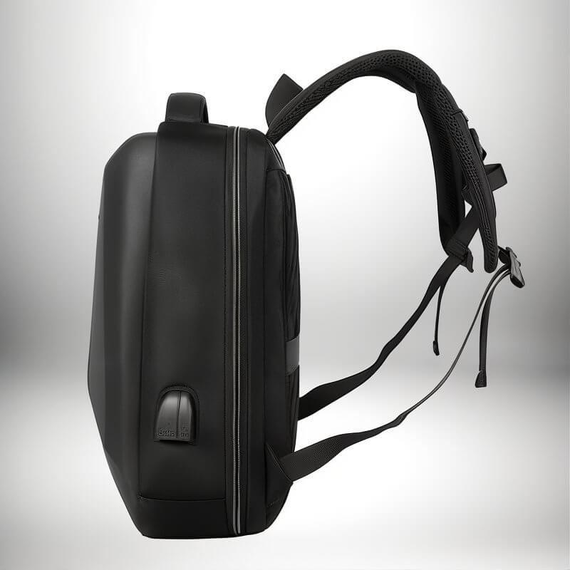 Un sac à dos coque rigide noir est présenté de côté, avec un port USB intégré et des bretelles rembourrées.