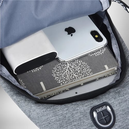 Vue de l’intérieur d’un sac de sport bandoulière sur fond gris, il contient un téléphone, un chargeur, une pile et un carnet avec des arbres illustrés. L’intérieur est bleu clair. Le sac est fermé par une fermeture éclair noire.
