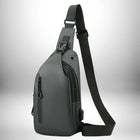 Un sac banane homme luxe gris foncé, en forme de goutte d'eau, avec une poche zippée verticale à l'avant et une sangle réglable, se trouve sur un fond dégradé.
 — vue 6
