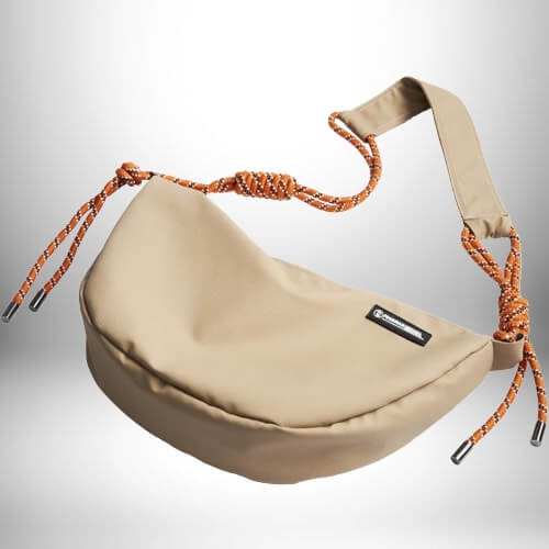 Un petit sac de sport homme beige en forme de croissant avec une bandoulière faite de cordes orange et beiges. Il y a une petite étiquette noire sur le devant du sac.