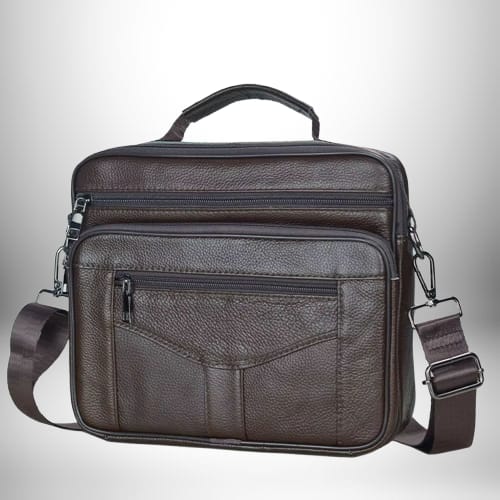 Un sac bandoulière homme cuir souple de couleur marron avec plusieurs poches zippées et une poignée sur le dessus. La bandoulière est réglable et est fixée sur le sac avec des mousquetons.
