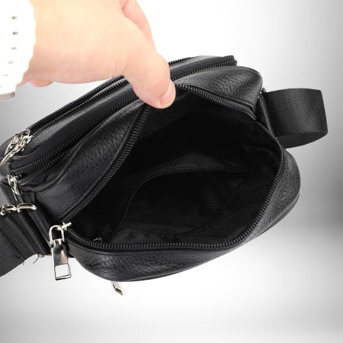 Gros plan d'un sac bandoulière cuir noir homme​ ouvert par une main humaine, révélant l'intérieur noir.