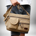 Un homme porte un sac de ville homme en toile de couleur beige. Le sac comporte de nombreuses poches et une bandoulière. — vue 4