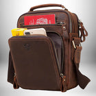 Image d'un sac de ville homme marron en cuir avec plusieurs poches, une poignée sur le dessus et une bandoulière. On peut voir un passeport, un téléphone et un paquet de cigarettes à l'intérieur.
 — vue 5