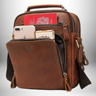 Un sac de ville homme en cuir marron avec de nombreuses poches zippées, dont une à l'avant qui est ouverte et révèle un téléphone portable, un paquet de cigarettes et un passeport. La poignée supérieure et la bandoulière sont également visibles.
 — vue 6