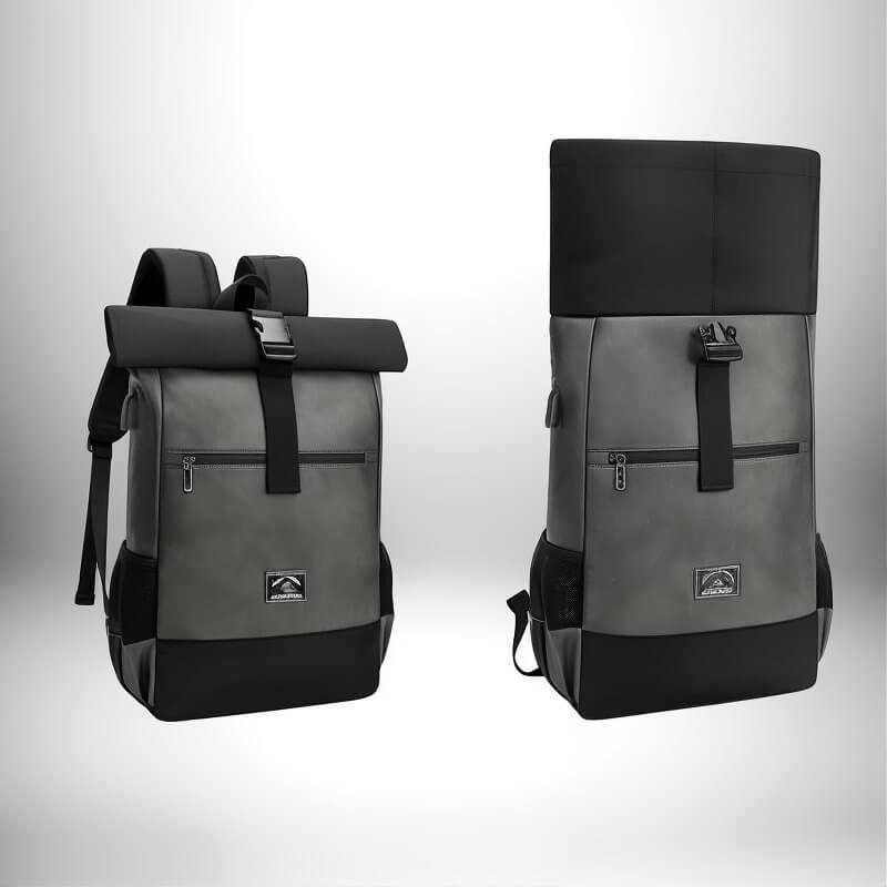 Two modern-looking backpacks are displayed against a white background. The backpacks are in a gray/charcoal color scheme with black accents. The left backpack is closed with a roll-top design, and a black strap with a buckle. The right backpack is open with the roll part in the up position.