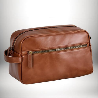 Une trousse de toilette de voyage en cuir marron, avec une fermeture éclair et une poignée latérale, posée sur une surface blanche.