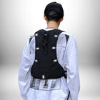 Une personne vue de dos, portant un chapeau noir et une chemise blanche à manches longues avec un imprimé graphique noir et blanc. Elle porte un gilet noir de style sac à dos avec des bandes réfléchissantes. L'arrière-plan est blanc légèrement ombragé.
 — vue 3