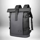 Un sac à dos noir de style urbain avec une fermeture à rabat. Le sac a des bretelles, des sangles sur le côté et une boucle sur le rabat.
 — vue 1